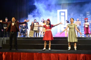 Annie, Mr. Warbuck, and Grace Ferrel singing on the stage.