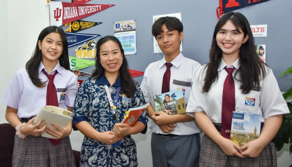 Three IB Diploma Programme Students with a teacher, holding universities brochures