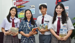 Three IB Diploma Programme Students with a teacher, holding universities brochures